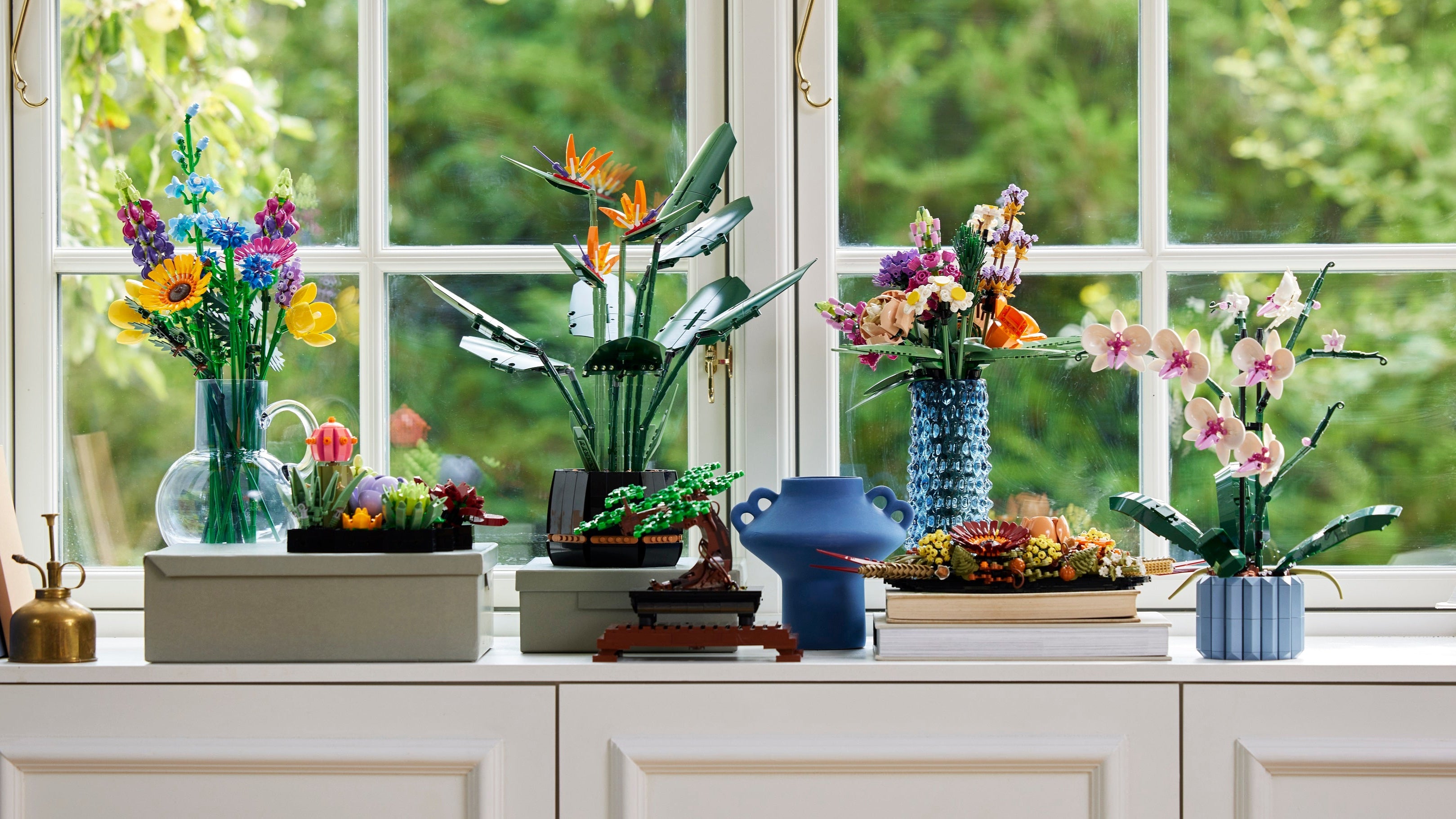 Decorative arrangement of flowers and vases on a windowsill with a blurred green outdoor background.